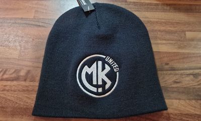 A dark blue or black knit beanie resting on a wooden surface, featuring a white, circular embroidered MK UNITED logo.