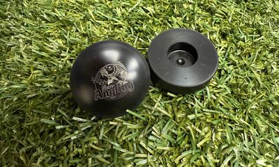 Two black, circular fishing accessories resting on artificial green grass. One is positioned face-up, displaying a smooth domed top engraved with the 'Nero Angling' leaping fish logo. The other is turned over, revealing a hollow, recessed underside.